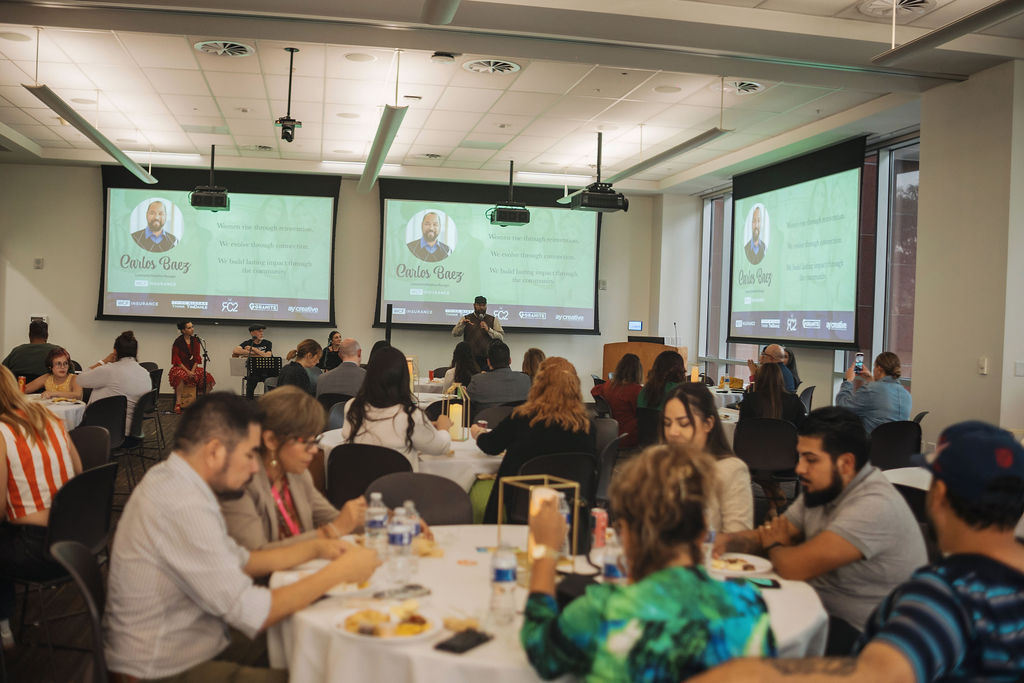 Attendees at dinner as Carlos Baez is introduced on screen